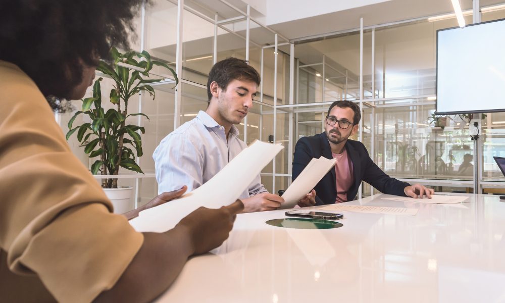 3 mixed Latin business people meeting in an office reading a contract with a lawyer.