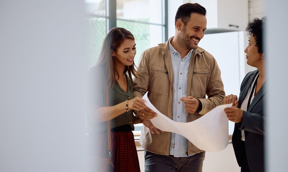 Happy couple of buyers and real estate agent analyzing housing plans.